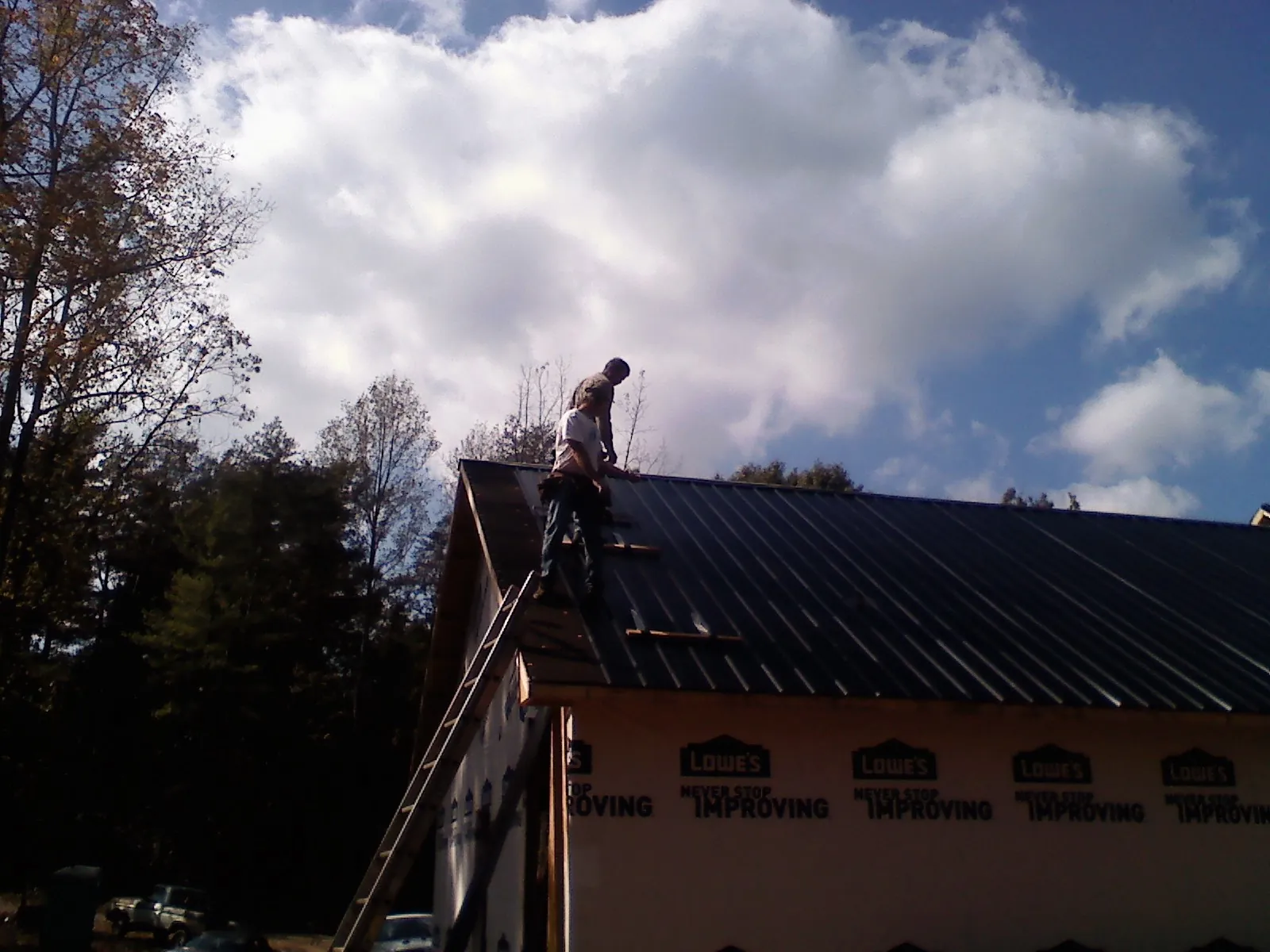 Roofer fastening dark metal panels high against a cloudy sky, from a Roof Inspection job in Bloomingburg